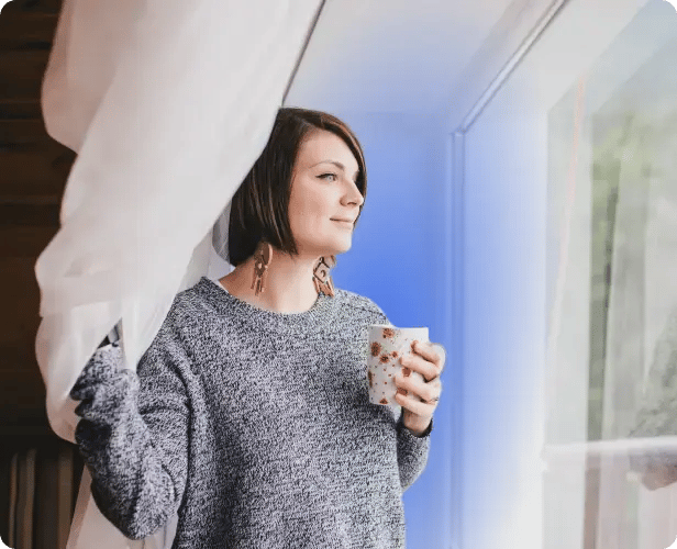 woman looking out window drinking coffee