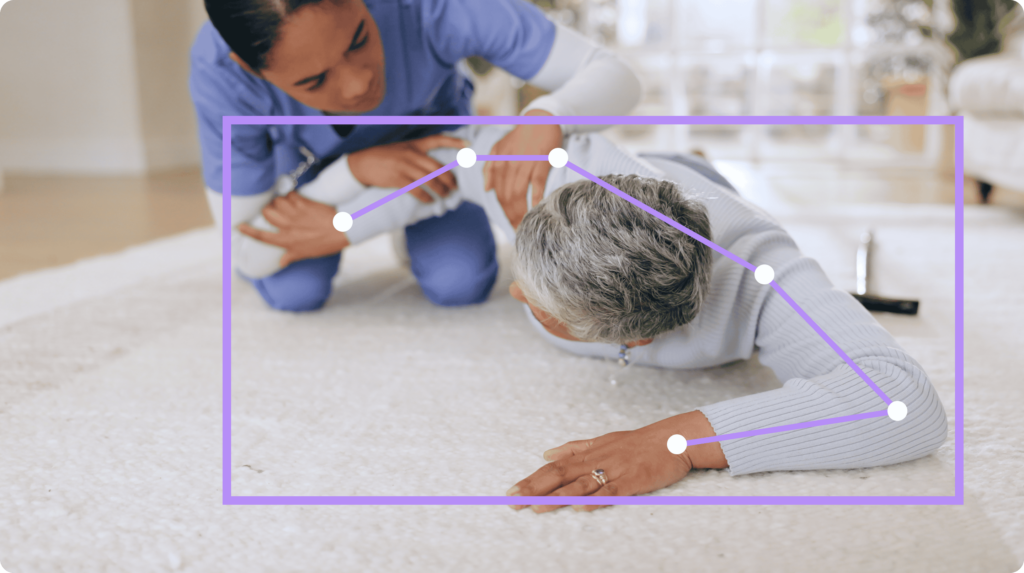 Older person laying on the floor receiving assistance from a nurse or caregiver.